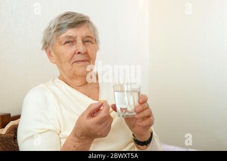 An elderly woman is going to swallow a medicine, a pill and drink it with water. Stock Photo