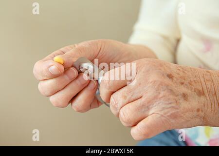 An elderly woman is going to swallow a medicine, a pill and drink it with water. Closeup of a hand with a tablet. Stock Photo