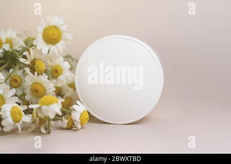 Facial or body cream and many chamomiles flowers on the beige background. Stock Photo