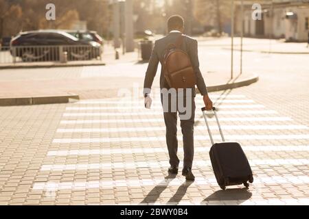 Businessman Crossing Road Walking With Suitcase In City, Back View Stock Photo