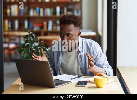 Frustrated African American man with laptop studying or working in coffee shop Stock Photo