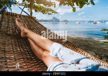 Feet of adult woman relaxing in a hammock on the beach during summer holiday. Stock Photo