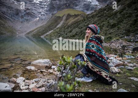 Beautiful blonde woman sitting by a blue lake in the middle of the mountains in Peru. Turquoise water lake. Stock Photo