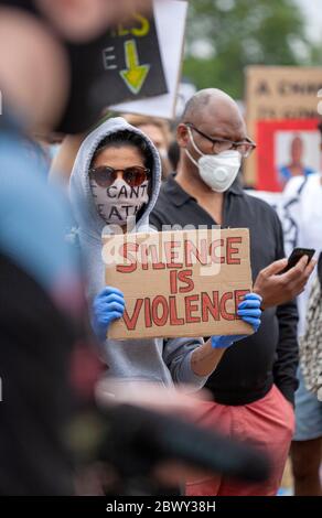 Woman, wearing sunglasses and a face mask, holds a sign up that says 'Silence is violence' during the Black Lives Matter UK protest march. London, UK Stock Photo