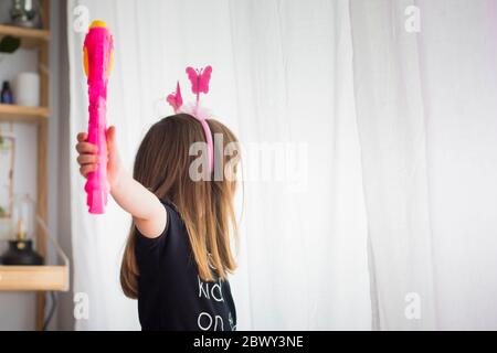 Little child girl, at home playing in disguise wearing  pink antennas and holding a toy magic wand. Gender equality and feminism concept, background. Stock Photo