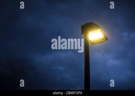 Lit street lamp at twilight with moody blue sky and rain falling. Gloomy and spooky background with copy space on the left. Stock Photo