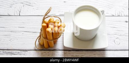 Cup of milk and breadsticks tied with string on a wooden background. Healthy snack. Stock Photo
