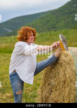 Mature woman on hay haystack in field Stock Photo