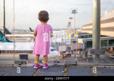 the kid looks at the planes at the airport and is waiting for boarding. back view Stock Photo