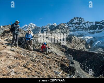 Nepal. Trek to Mera Peak. European trekkers take a break to absorb the view above the Hinku valley and settlement of Share en-route to Mera Peak. Stock Photo