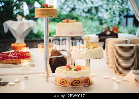 White flower decorated separate-tiered wedding cake standing on festive table inside room. Wedding day concept. Stock Photo