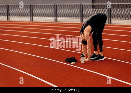 Young handsome man doing stretching before running in the stadium wearing black sport clothes at summer Stock Photo