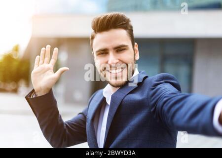 Cheerful entrepreneur waving his hand while taking selfie at downtown area Stock Photo