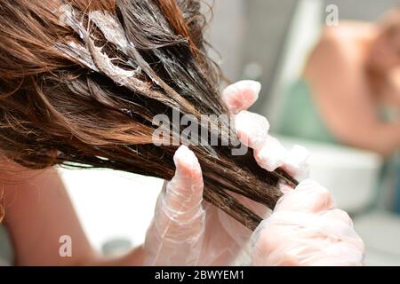 Young woman dyes her hair at home. The girl coloring her hair in her own bathroom. Quarantine, home hair care, stay at home concept. Stock Photo