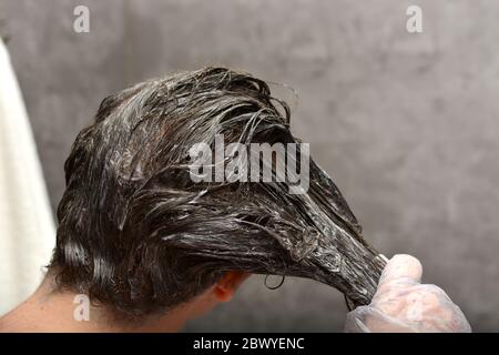 Young woman dyes her hair at home. The girl coloring her hair in her own bathroom. Quarantine, home hair care, stay at home concept. Stock Photo