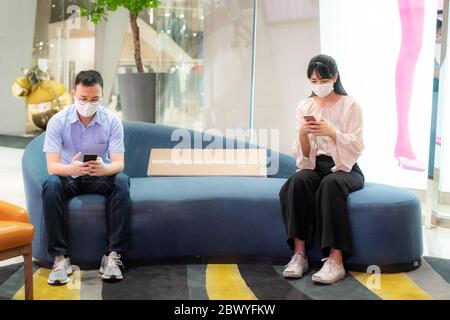 Two Asian young man and woman wearing mask and talking with friend while sitting distance of 6 feet distance protect from COVID-19 viruses for social Stock Photo