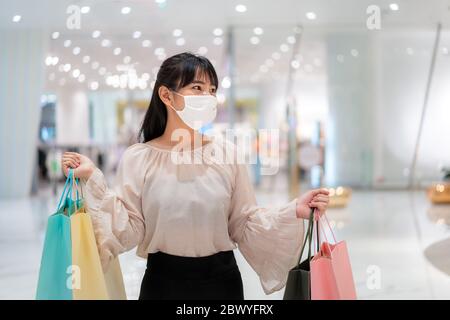 Asian woman wearing mask over her face while walking at shopping mall with shopping bag for healthcare and prevention from coronavirus, Covid19 influe