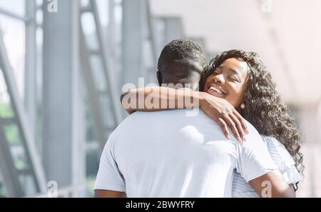 Long-awaited meeting. Happy african american woman embracing her husband in airport Stock Photo