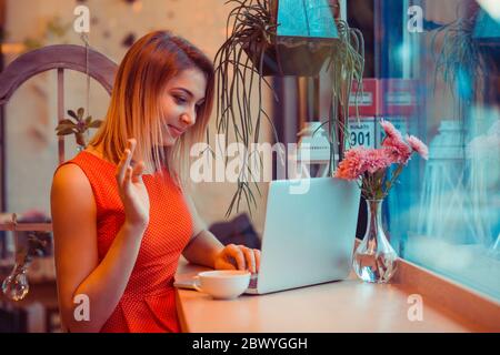 Smiling student woman, freelancer having a video call, online web interview on a laptop in her home kitchen, near window or in a coffee shop, trendy c Stock Photo