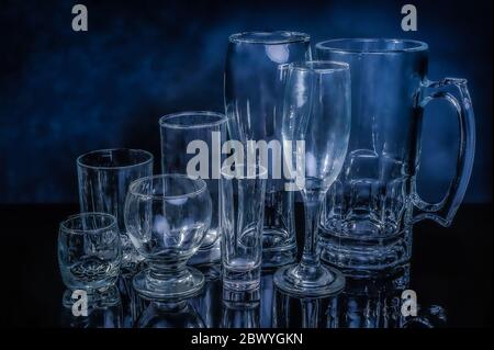 glass drinkwares and stemwares of different shapes and sizes stand side by side on an isolated black background with reflection Stock Photo