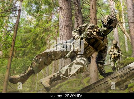 Photo of a fully equipped soldiers jumping and running with rifles in forest. Stock Photo