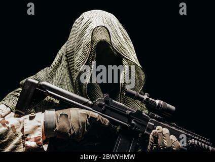 Isolated photo of a fully equipped camouflaged soldier in tectical net scarf with tactical vest and gloves holding sniper rifle. Stock Photo