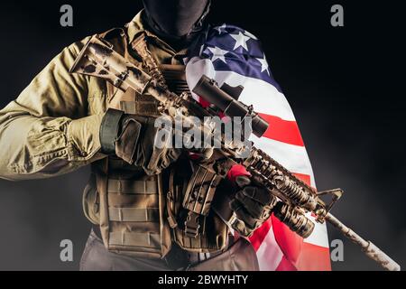 Photo of a fully equipped soldier in armor vest and rifle standing with american flag. Stock Photo