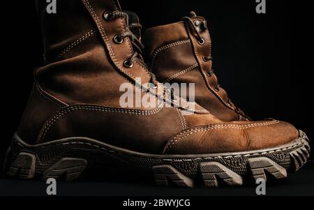 Photo of brown military tactical boots standing on black surface background profile view. Stock Photo