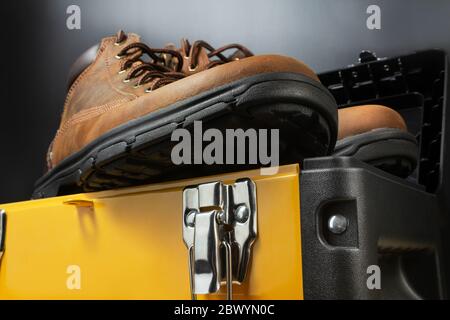 Worker leather boots standing on yellow toolbox on black background. Stock Photo