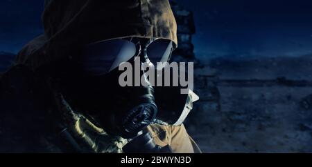Photo of a desert post-apocalyptic soldier in tactical jacket, gas mask and armor face standing on night wasteland background side view. Stock Photo