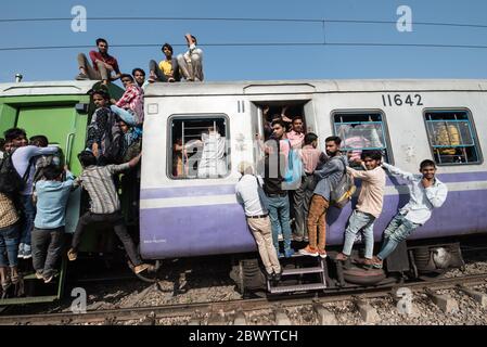 Commuters hang in between rail cars and sit on the roof of an overcrowded Indian Railways train, Noli Railway Station near Ghaziabad, Delhi, India. Stock Photo