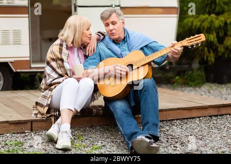 Retired couple with guitar singing together near their motorhome at campsite Stock Photo