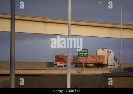 Lumber or timber truck on interstate highway overpass with green Next Exit sign for Mandela Parkway.  Road transportation. West Oakland, California. Stock Photo