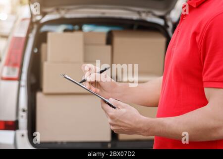 Courier are notes to tablet delivered parcel, close up, car with boxes near Stock Photo