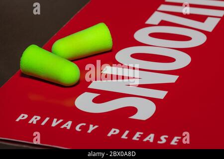 Earplugs on red privacy / snoozing sign. Snoozing sign reads 'Privacy please'. Sign and one of the ear plugs are in soft focus. Close-up shot. Stock Photo