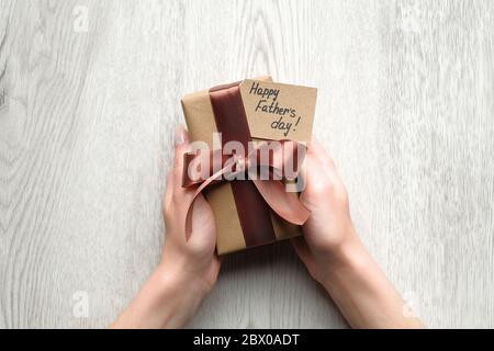 Womans hands holding gift box wrapped festive ribbon and label with text Happy Father's Day on wooden table, top view. Present for daddy, Fathers Day Stock Photo