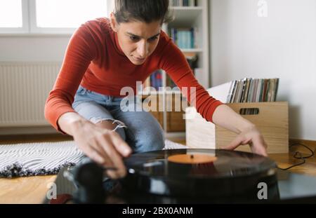 Smiling woman playing favorite vinyl record on turntable Stock Photo