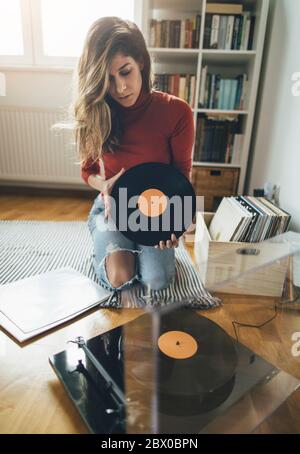 Young woman sitting on floor with vinyl record. Playing music on turntable, leisure time, hobbie Stock Photo