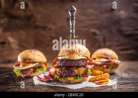 A knife-stabbed double beef burger with chips and chilli, more burgers in the back in a dark environment Stock Photo