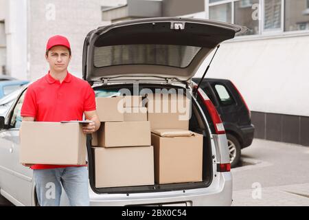 Express delivery to home. Courier holds box near open car with parcels Stock Photo
