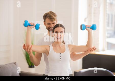 Smiling woman holding dumbbells and her husband helping her Stock Photo