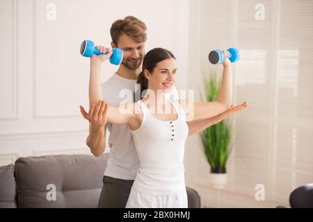 Smiling woman holding dumbbells and her husband supporting her Stock Photo