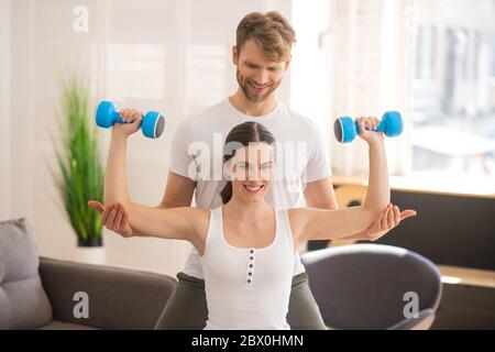 Smiling woman working on her muscles and her husband helping her Stock Photo