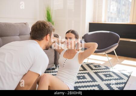 Smiling woman working on her abs and her husband helping her Stock Photo