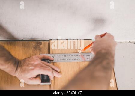 Worker measuring and marking laminate for cutting - installing floating floor - close-up on hands - home renovation concept Stock Photo