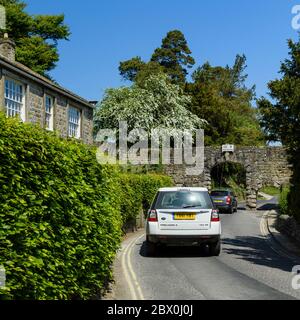 2 cars on country lane approaching narrow stone archway (arches, headroom warning sign 10' 9'')  - B6160, Bolton Abbey village, Yorkshire, England, UK Stock Photo