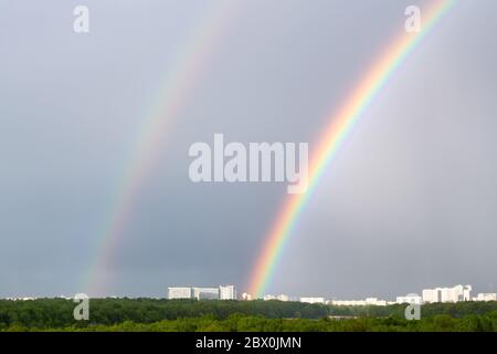 double rainbow over green city park and urban houses on horizon on spring day Stock Photo