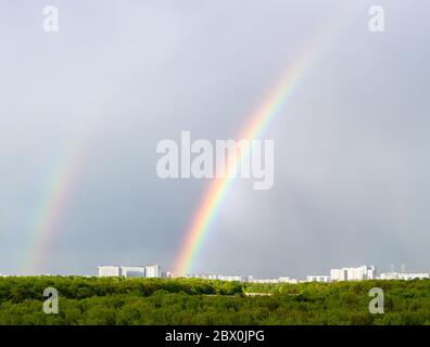 double rainbow over green city park and residential houses on horizon on spring day Stock Photo