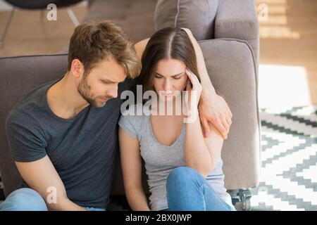 Young pretty woman looking sad while her husband hugging her Stock Photo