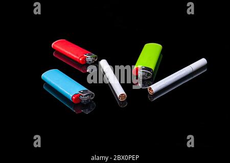 white filter cigarettes and plastic gas lighters of different colors on an isolated black background with reflection Stock Photo